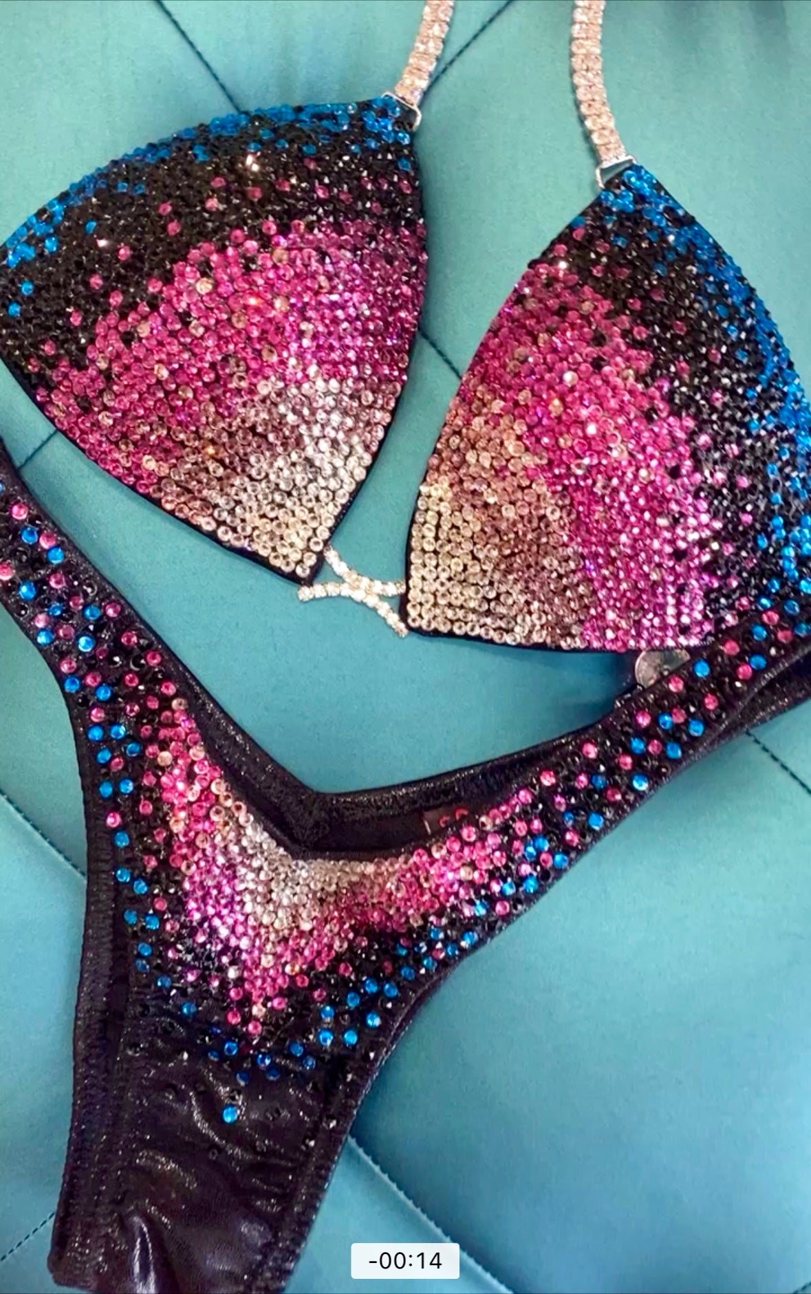A two-piece figure competition swimsuit in black and fuchsia with ombre rhinestone design, displayed on a flat surface.